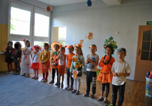 Grupa dzieci w jesiennych przebraniach stoi ustawiona w rzędzie. Ujęcie 1